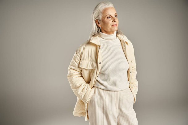 красива і сіра жінка середнього віку в елегантному вбранні позує на сірому фоні - Фото, зображення