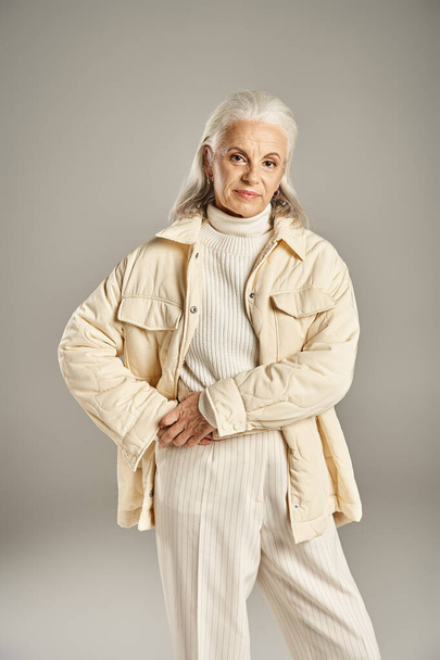 красивая и седовласая женщина средних лет в элегантной одежде, позирующая на сером фоне - Фото, изображение
