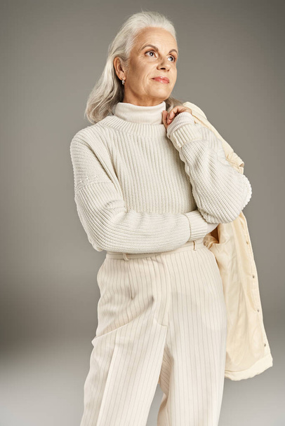 gyönyörű és ősz hajú középkorú nő elegáns öltözékben pózol szürke háttér - Fotó, kép