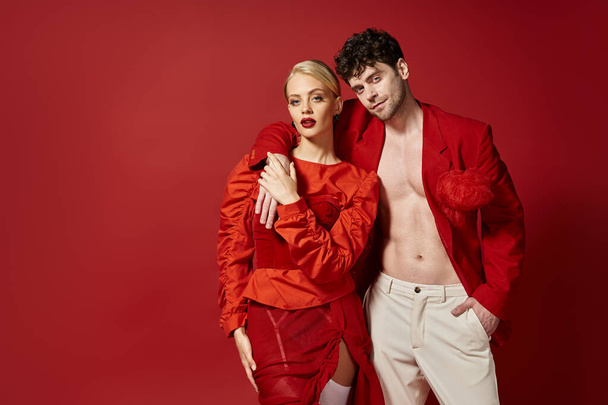 stylish man in red blazer and white pants posing while putting hand around neck of blonde woman - Photo, Image