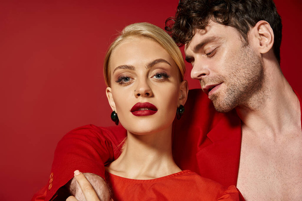 hombre guapo poniendo la mano alrededor del cuello de la atractiva mujer rubia con labios rojos en vibrante telón de fondo - Foto, imagen