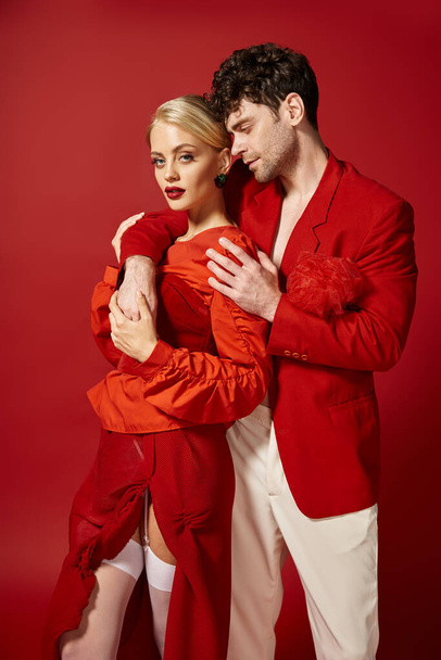handsome man putting hand around neck of blonde woman with red lips on vibrant backdrop, fashion - Photo, Image