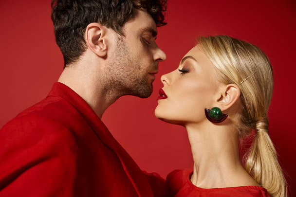 vista lateral del hombre guapo posando con atractiva mujer rubia con labios rojos sobre un fondo vibrante - Foto, imagen