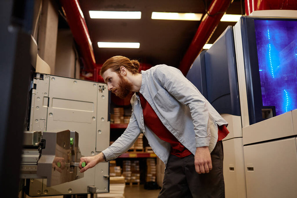Retrato de vista lateral de un joven haciendo un control de mantenimiento de las máquinas de impresión industrial en la tienda - Foto, Imagen