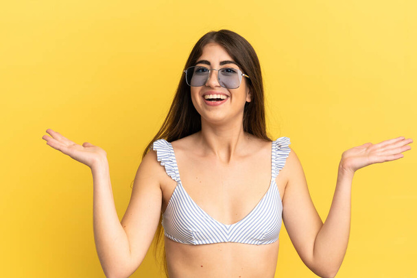 Young caucasian woman in swimsuit in summer holidays isolated on yellow background with shocked facial expression - Photo, Image