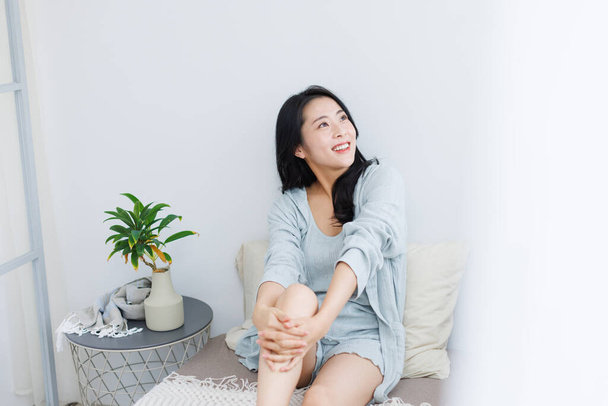portrait of smiling young Asian woman sitting on the bed at home  - Photo, Image