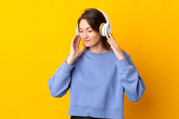 Jeune Irlandaise isolée sur fond jaune écoutant de la musique - Photo, image