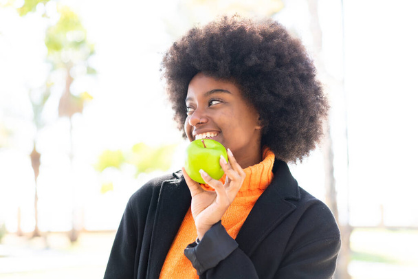African American girl at outdoors holding an apple with happy expression - Photo, Image
