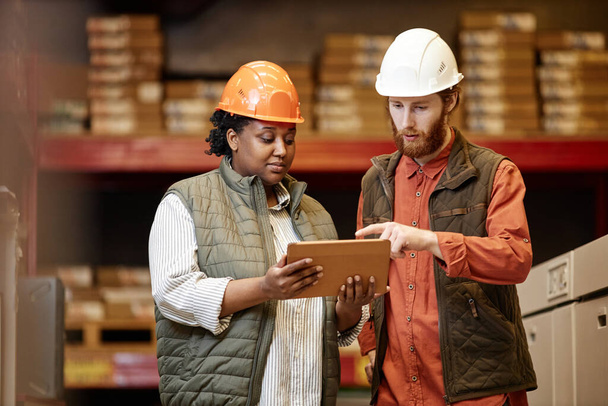 Porträt von zwei Arbeitern, die Harthüte in der Fabrik tragen und ein digitales Tablet benutzen - Foto, Bild