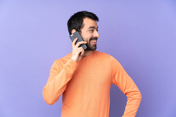 Кавказький красивий чоловік над ізольованим фіолетовим тлом, що тримає розмову з мобільним телефоном з кимось - Фото, зображення