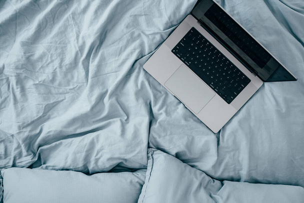 Kannettavan tietokoneen aamulla sininen lakanat sänky. Töitä kotoa. Freelance-käsite - Valokuva, kuva
