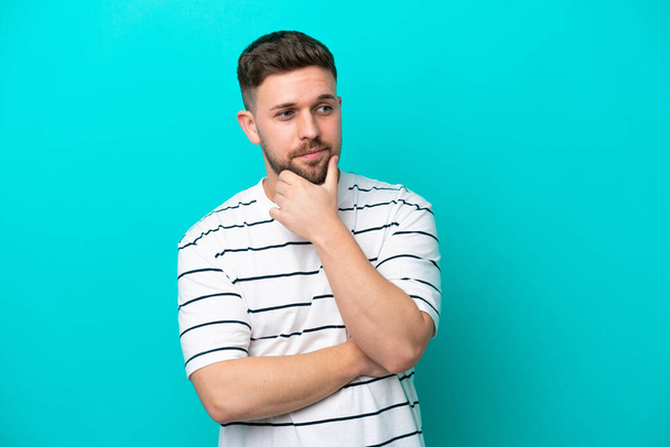 Young caucasian man isolated on blue background looking to the side and smiling - Photo, Image