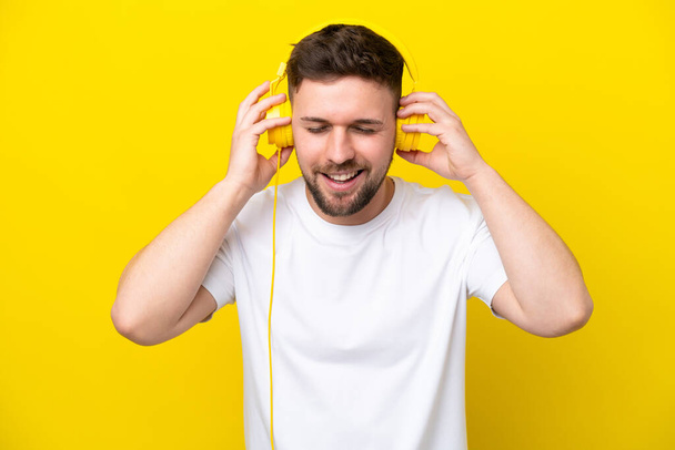Junger kaukasischer Mann isoliert auf gelbem Hintergrund Musik hörend - Foto, Bild
