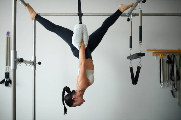 Fit strong young woman doing upside down exercise in special machine - Photo, Image