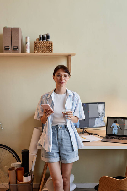 Verticaal portret van creatieve jonge vrouw als digitale 3D-ontwerper glimlachend op camera door kantoor thuis - Foto, afbeelding