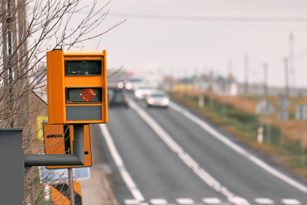 Κάμερα ταχύτητας εξοπλισμένη με ραντάρ παρακολουθεί την κυκλοφορία σε δρόμο, αναβοσβήνει κίτρινο φως όταν πιάνει αυτοκίνητο που υπερβαίνει το όριο ταχύτητας και χρησιμοποιεί τεχνολογία για την αναγνώριση του οχήματος και την επιβολή του νόμου. - Φωτογραφία, εικόνα