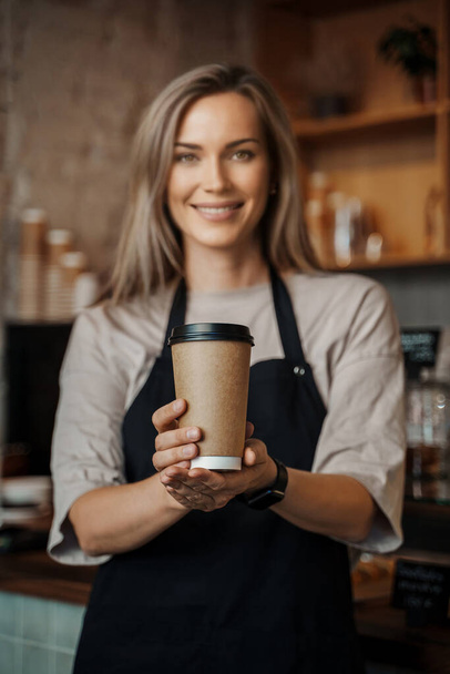 Ein Barista in einem Coffeeshop präsentiert eine wiederverwertbare Kaffeetasse zum Mitnehmen, die einen umweltbewussten Service hervorhebt - Foto, Bild