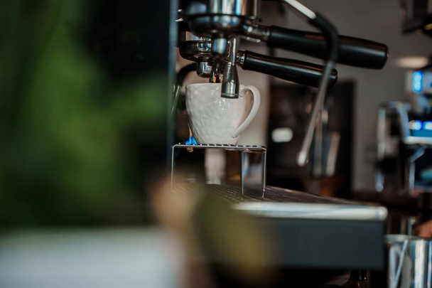 Μια περίπλοκη μηχανή espresso ρίχνει φρέσκο καφέ σε ένα κομψό λευκό κύπελλο, συλλαμβάνοντας την ουσία μιας ζωντανής καφετέριας - Φωτογραφία, εικόνα