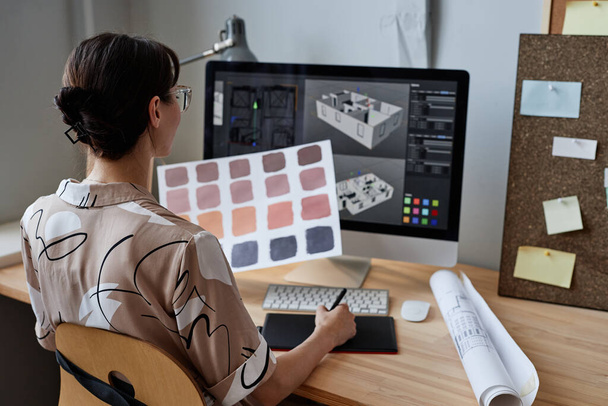 Γυναίκα σχεδιαστής κρατώντας δείγματα χρωμάτων, ενώ εργάζονται με τον υπολογιστή στο χώρο εργασίας - Φωτογραφία, εικόνα