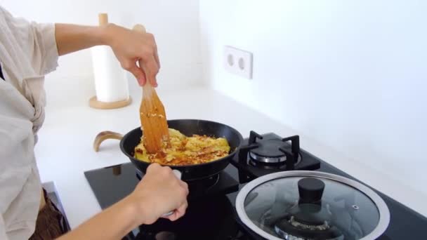 Nainen keittiössä tekee läksyjä. nainen sekoittaa munakas juustoa ja paista se paistinpannu liedellä. Kotimaan keittiön sisustus. Aamiainen valmistelu. - Materiaali, video