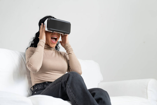Junge Frau nutzt Virtual-Reality-VR-Brille zu Hause für entscheidendes Online-Einkaufserlebnis. Virtual-Reality-VR-Innovation optimiert für weiblichen digitalen Unterhaltungsstil. - Foto, Bild