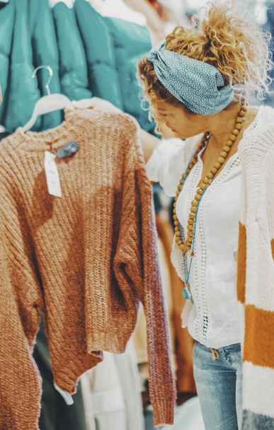 woman looking for garment in a store. Female people and fashion style business job or shopping activity. Trendy lady looking for sweater inside a shop during sales discount holiday season - Photo, Image