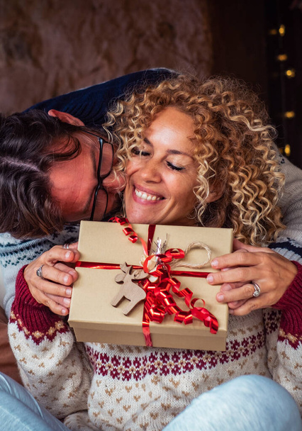 man doing surprise gift to a woman in Christmas Eve night celebration. Happy couple enjoy december holiday celebration at home together with love and joy. Concept of box present and Relationship - Photo, Image