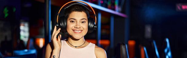 Молодая женщина излучает радость, слушая музыку через наушники в киберспортивном клубе, баннер - Фото, изображение