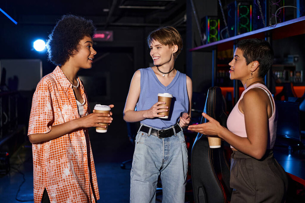 Monipuolinen ryhmä tyylikkäitä naisia, joilla on kahvikupit puhumassa ja kokoontumassa pimeässä huoneessa - Valokuva, kuva