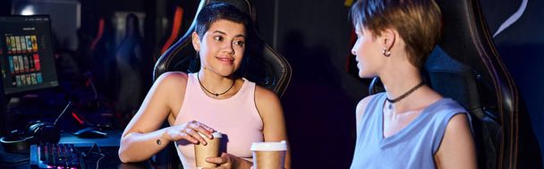 стильная женщина, держащая чашку кофе и глядя на свою подругу, игровой мир и баннер киберспорта - Фото, изображение
