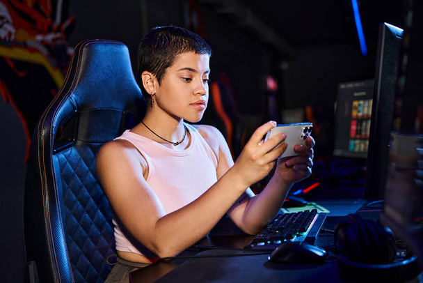 Keskittynyt nainen istuu mukavasti tietokoneellaan, kun hän sukeltaa digitaaliseen maailmaan puhelimitse. - Valokuva, kuva