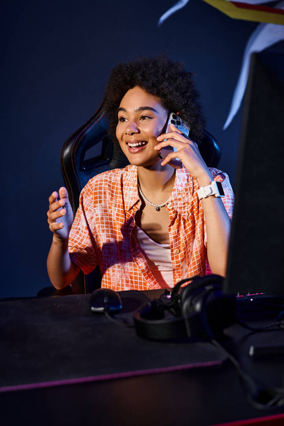 mulher negra alegre senta-se em seu computador e ter chamada telefônica perto do computador, clube ciberesporte - Foto, Imagem
