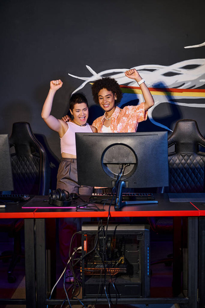 dwie międzyrasowe i radosne kobiety świętujące zwycięstwo po wygranej w pokoju gier, cybersport - Zdjęcie, obraz