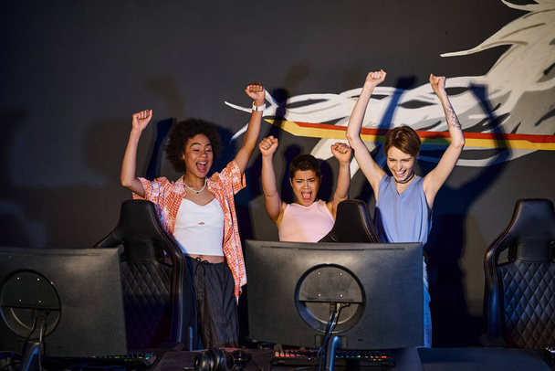 мультикультурные счастливые женщины, глядя на монитор компьютера и празднуя победу, подняли руки - Фото, изображение