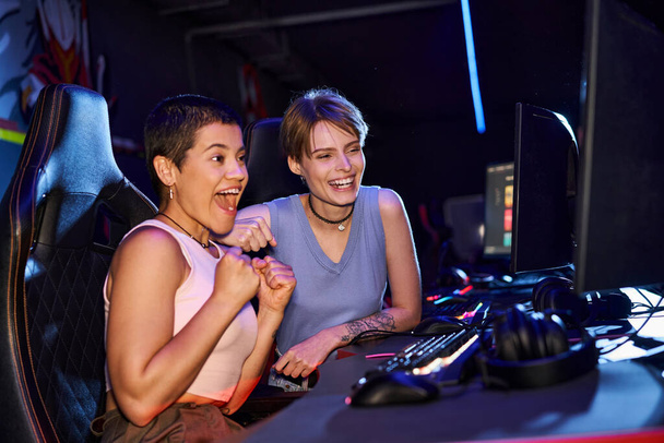 donne eccitate con tatuaggi che si concentrano su un gioco di cybersport nella sala del club di computer, giocatori femminili - Foto, immagini