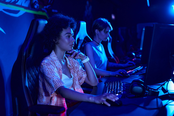 focus op ernstige Afrikaanse Amerikaanse vrouw gaming intens in een blauw-verlichte kamer, cybersport concept - Foto, afbeelding