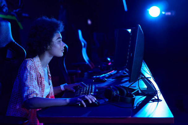 vista lateral de la mujer afroamericana enfocada que juega intensamente en una sala de luz azul, concepto de ciberdeporte - Foto, imagen