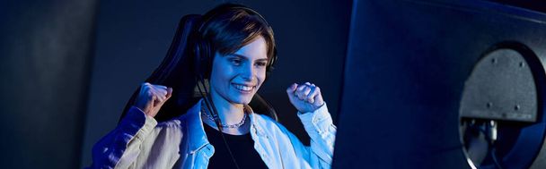 happy short-haired woman looking at computer in a blue-lit room, cybersport and gaming banner - Photo, Image