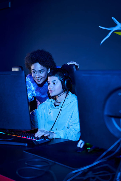 mujer joven en auriculares con micrófono jugando juego de ordenador cerca de amigo, cybersport - Foto, Imagen