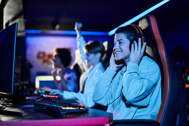 skupienie się na radosnej młodej kobiecie wygrywającej grę obok różnorodnych przyjaciółek, graczy cybersportu - Zdjęcie, obraz