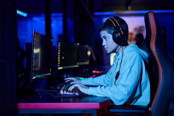 Konzentration auf konzentrierte junge Frau, die in einem blau beleuchteten Raum spielt, Cybersport-Spielerin - Foto, Bild