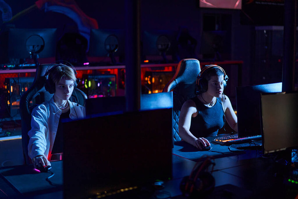 сфокусовані геймери в навушниках, які дивляться на монітори, граючи в багатокористувацьку комп'ютерну гру, кіберспорт - Фото, зображення