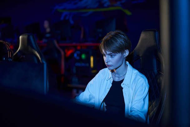 сфокусированная женщина смотрит на монитор во время игры в многопользовательскую компьютерную игру, женщина-геймер рядом с ПК - Фото, изображение