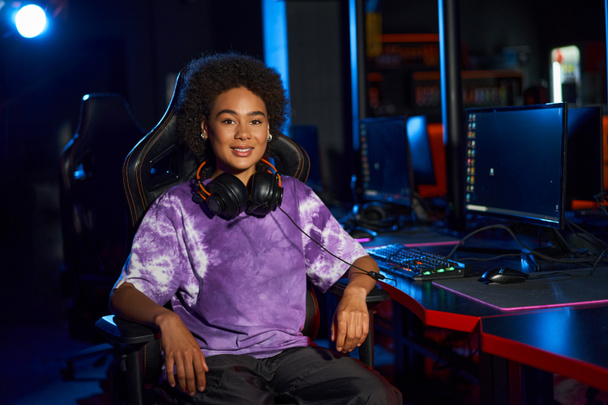 щаслива афроамериканська жінка-геймер з навушниками, що сидять на зручному ігровому кріслі, кіберспорт - Фото, зображення