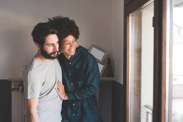 Молодая многонациональная пара обнимается, улыбаясь дома   - Фото, изображение