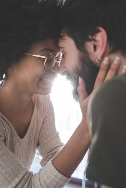 Joven pareja multiétnica abrazándose sonriendo juntos en casa - Foto, imagen