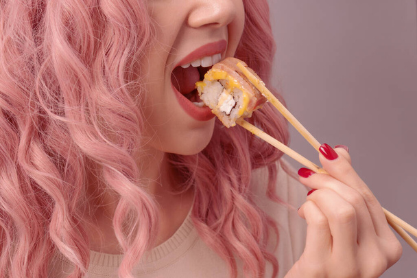 Mujer joven con uñas rojas y pelo rosa está comiendo sushi de cerca. - Foto, Imagen