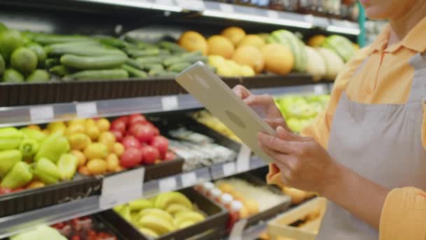 Przycięte ujęcie nierozpoznawalnej pracowniczki supermarketu sprawdzającej ilość artykułów spożywczych i umieszczającej informacje w tablecie cyfrowym podczas porannego audytu produktu - Materiał filmowy, wideo
