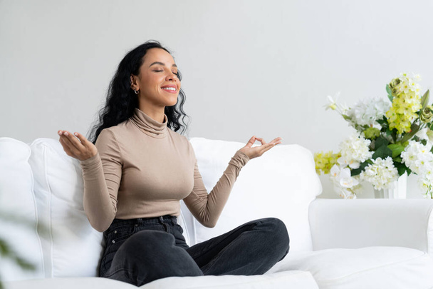 Νεαρή Αφροαμερικάνα πρακτική κρίσιμη προσεκτική διαλογισμό στο σπίτι σαλόνι για τη βελτίωση της ψυχικής υγείας δύναμη και ειρηνική όμορφη διαβίωση - Φωτογραφία, εικόνα