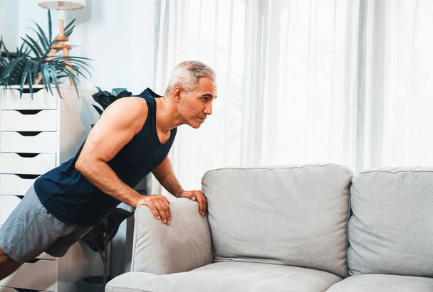 Homme âgé sportif et actif utilisant des meubles pour cibler efficacement le muscle avec pousser vers le haut à l'exercice à la maison comme concept de mode de vie sain de corps de forme après la retraite. Clout - Photo, image